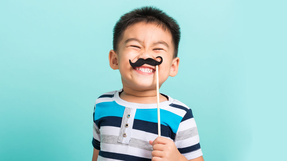 Cute boy posing with a mustache on a stick