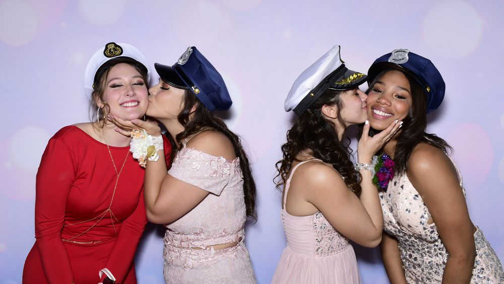 Girls kissing on cheeks in glam booth with glitter bokeh backdrop